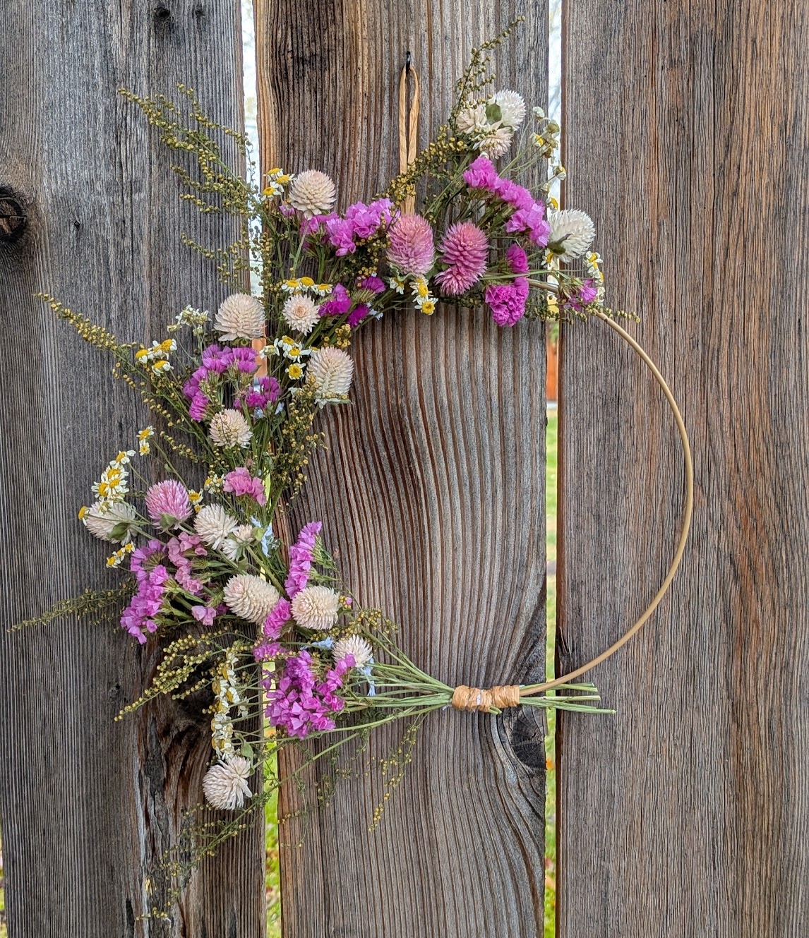 A dried flower wreath hanging on a weathered wooden fence